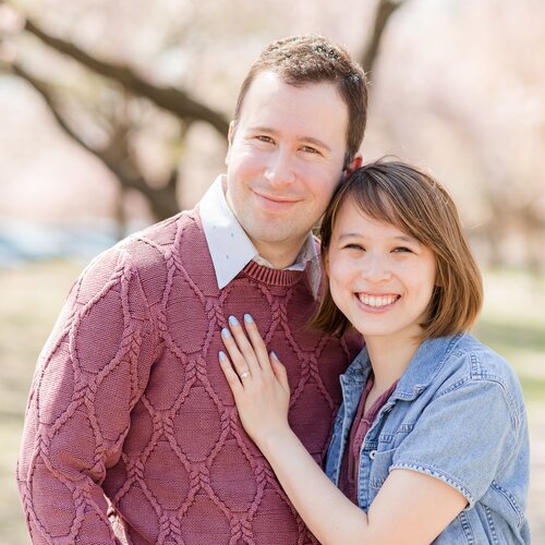 Julia and Nick standing shoulder-to-shoulder and smiling in front of a blossoming cherry tree
